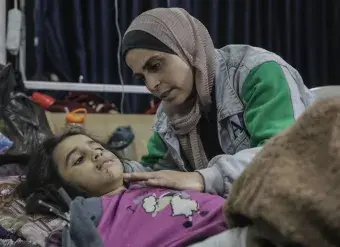 An injured child lays on a hospital cot while a women comforts her