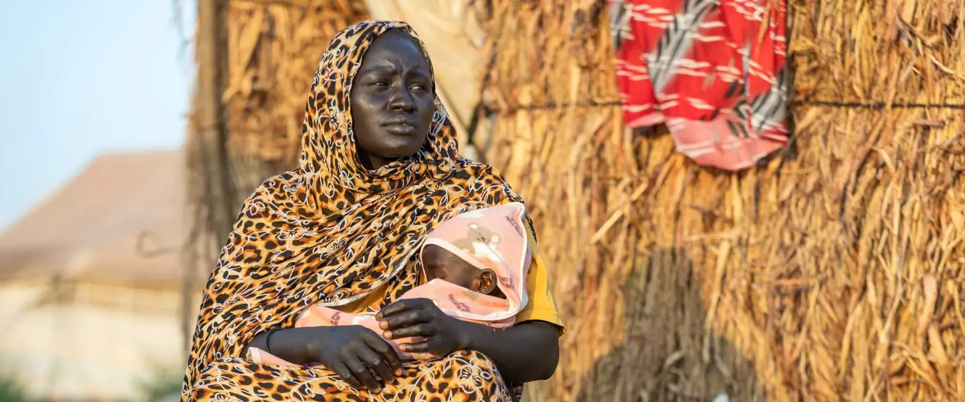 Malka, une mère déplacée, porte sa fille d'un an, Sahar, qui souffre de malnutrition aiguë sévère, devant sa maison au point de rassemblement des déplacés d'Elhoury dans l'État de Gedaref, en novembre 2024.